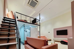 A modern interior with a staircase, a sofa, a flat-screen TV, and a ceiling fan. - Collection O Airport Rd Frmly Nano Pod (Surat)