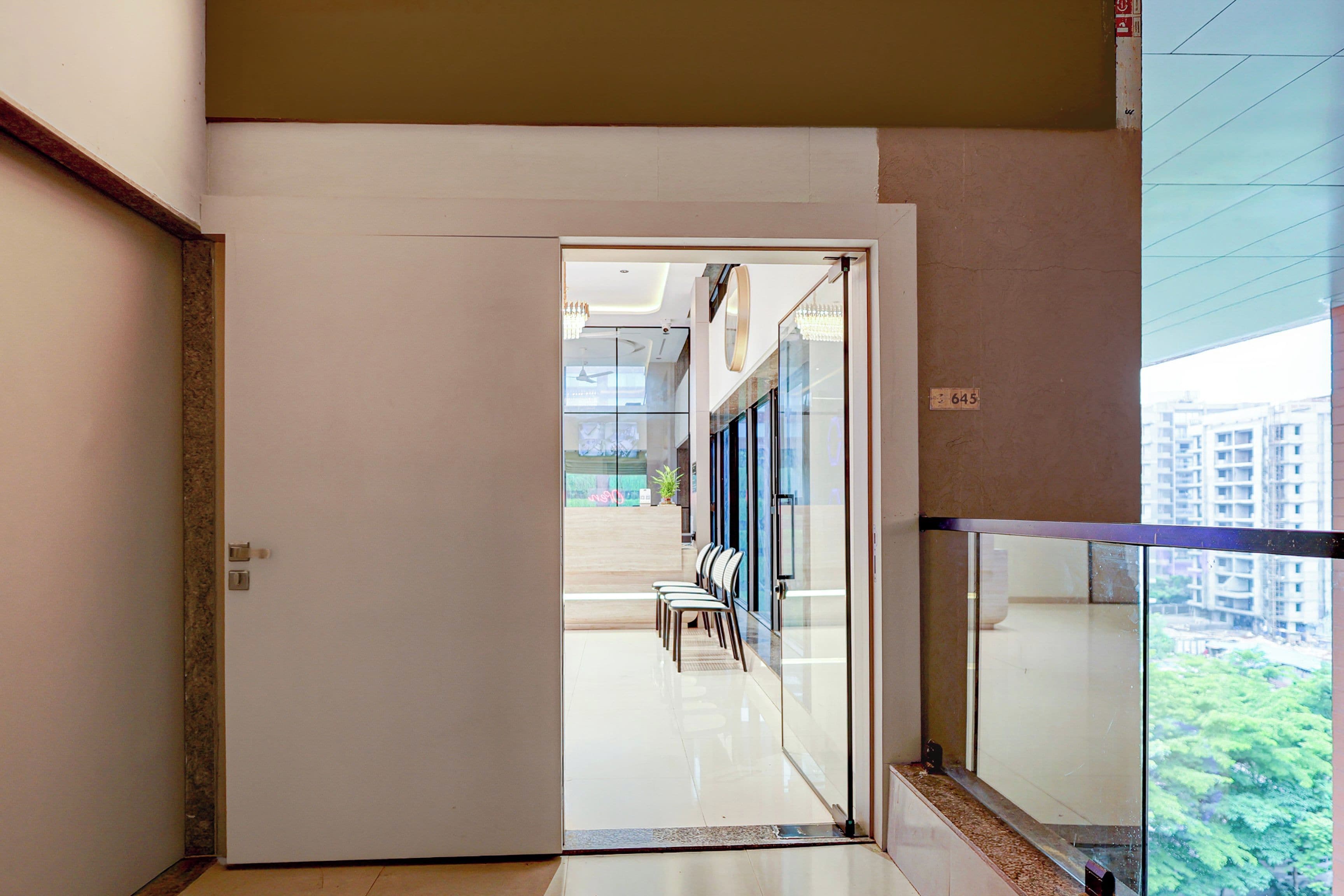 A hotel corridor with a glass door leading to a seating area with chairs and a table.