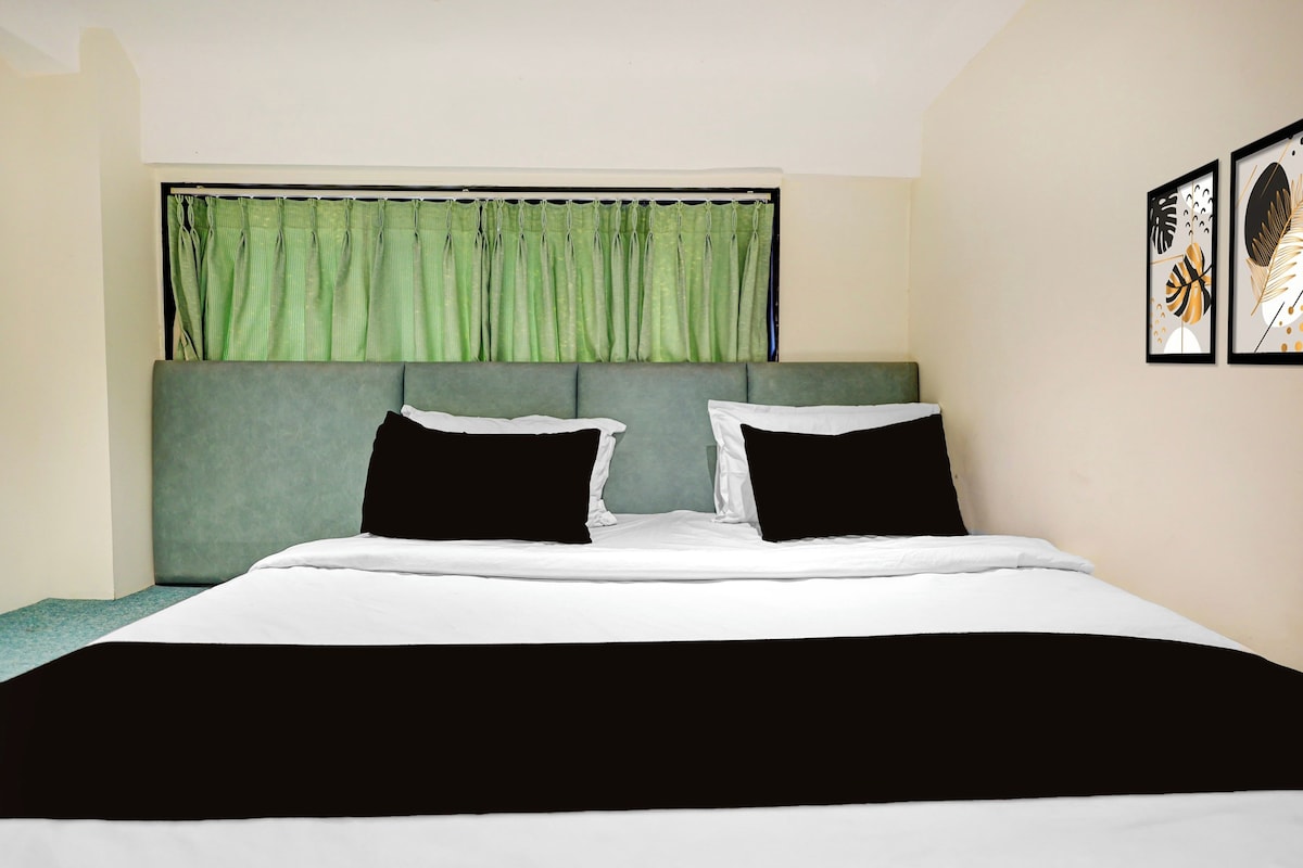 A bedroom with a bed, green curtains, and two framed pictures on the wall.