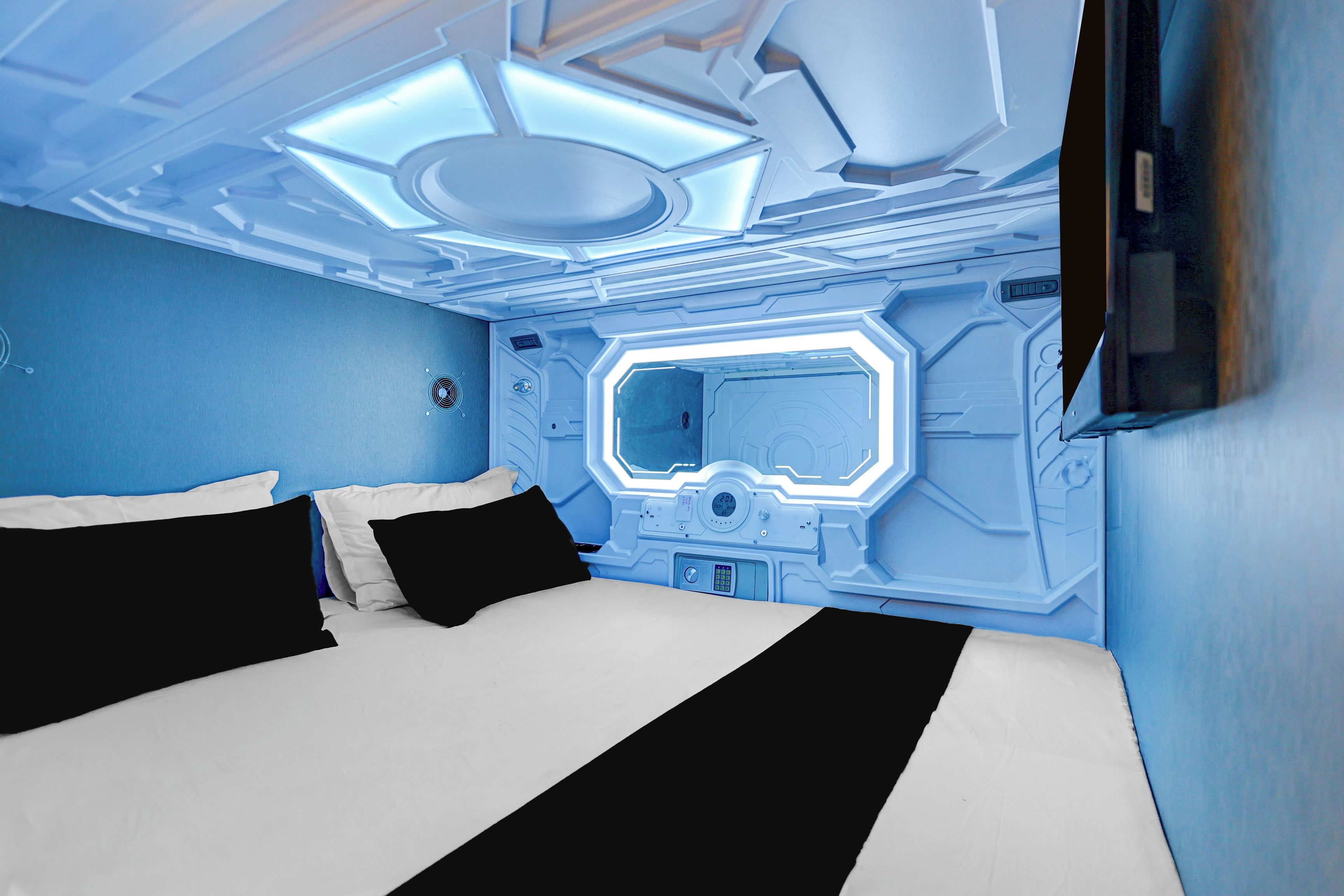 A room with a bed, a control panel, and a wall-mounted screen.