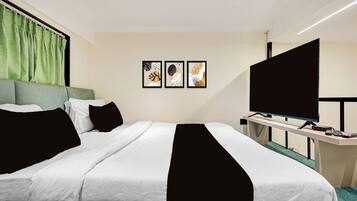 A hotel room with a large bed, a flat-screen TV, and three framed artworks on the wall.