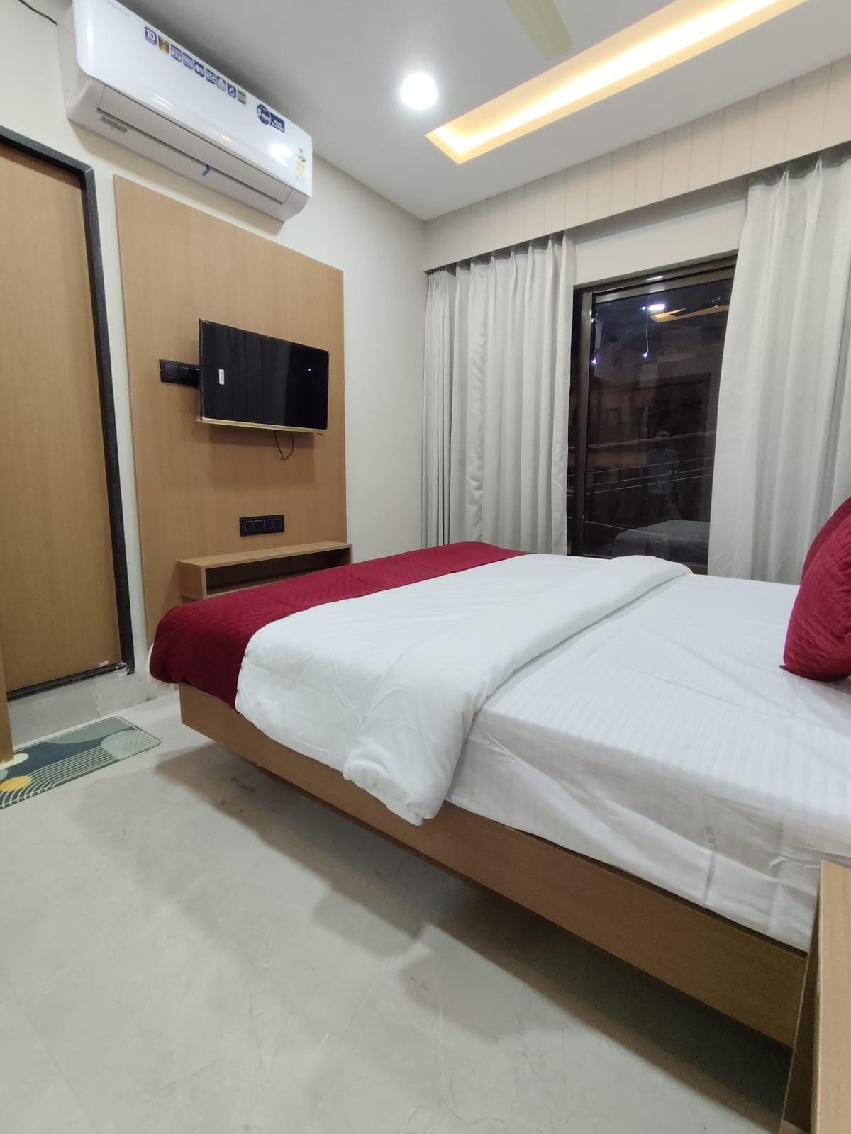 Habitació d'hotel amb un llit, un televisor fixat a la paret, una finestra amb cortines i un aparell d'aire condicionat.