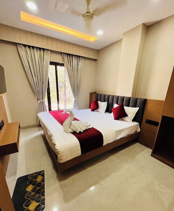 A hotel room with a large bed, a ceiling fan, and a view of the outdoors. - Hotel Jhala Palace (Ujjain)