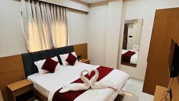 Una habitación de hotel con una cama, una mesita de noche, un espejo, un ventilador de techo y un televisor.