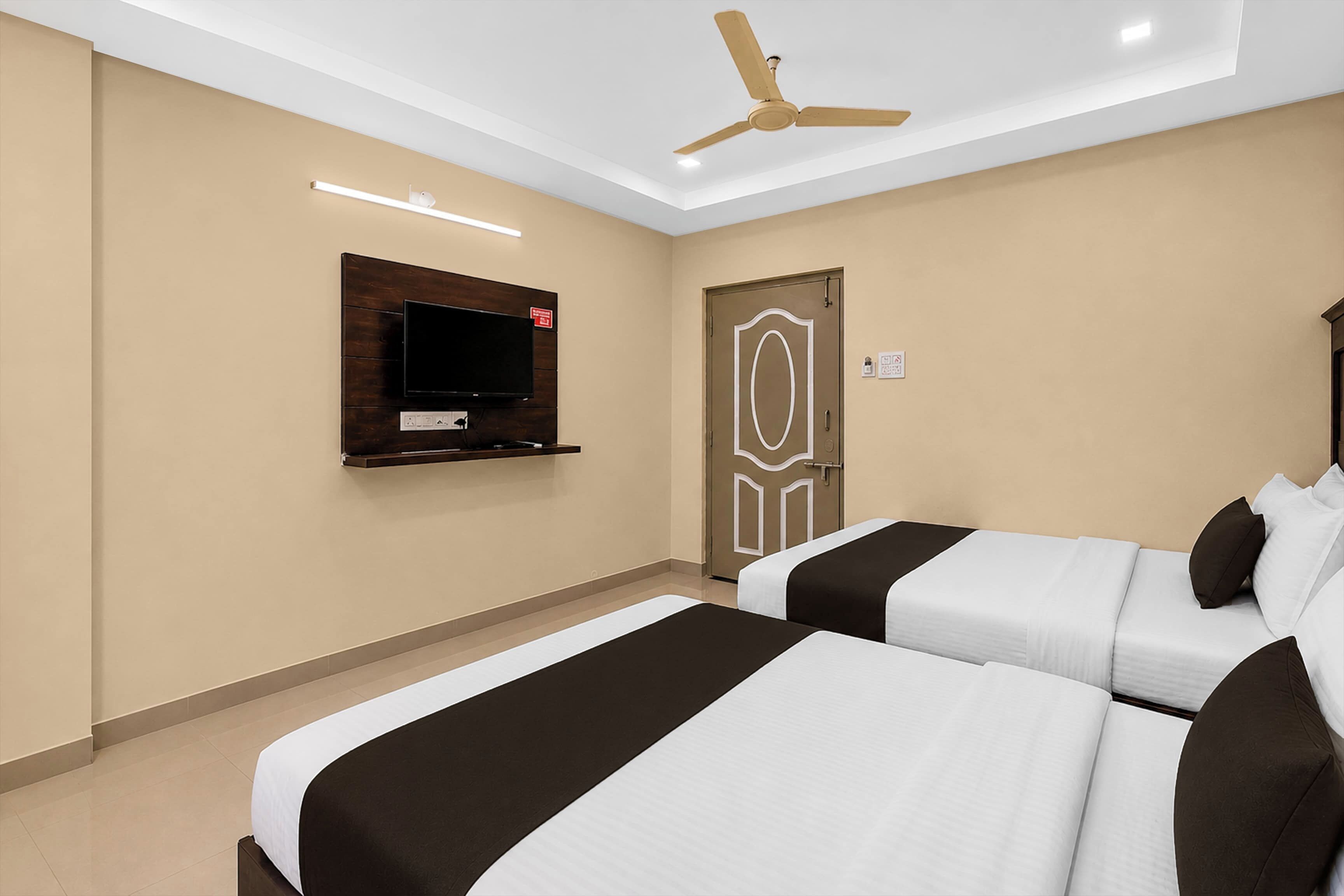 Ein Hotelzimmer mit zwei Betten, einem an der Wand befestigten Fernseher, einem Deckenventilator und einer Tür mit dekorativem Muster.