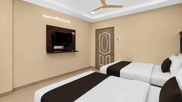 Ein Hotelzimmer mit zwei Betten, einem an der Wand befestigten Fernseher, einem Deckenventilator und einer Tür mit dekorativem Muster.
