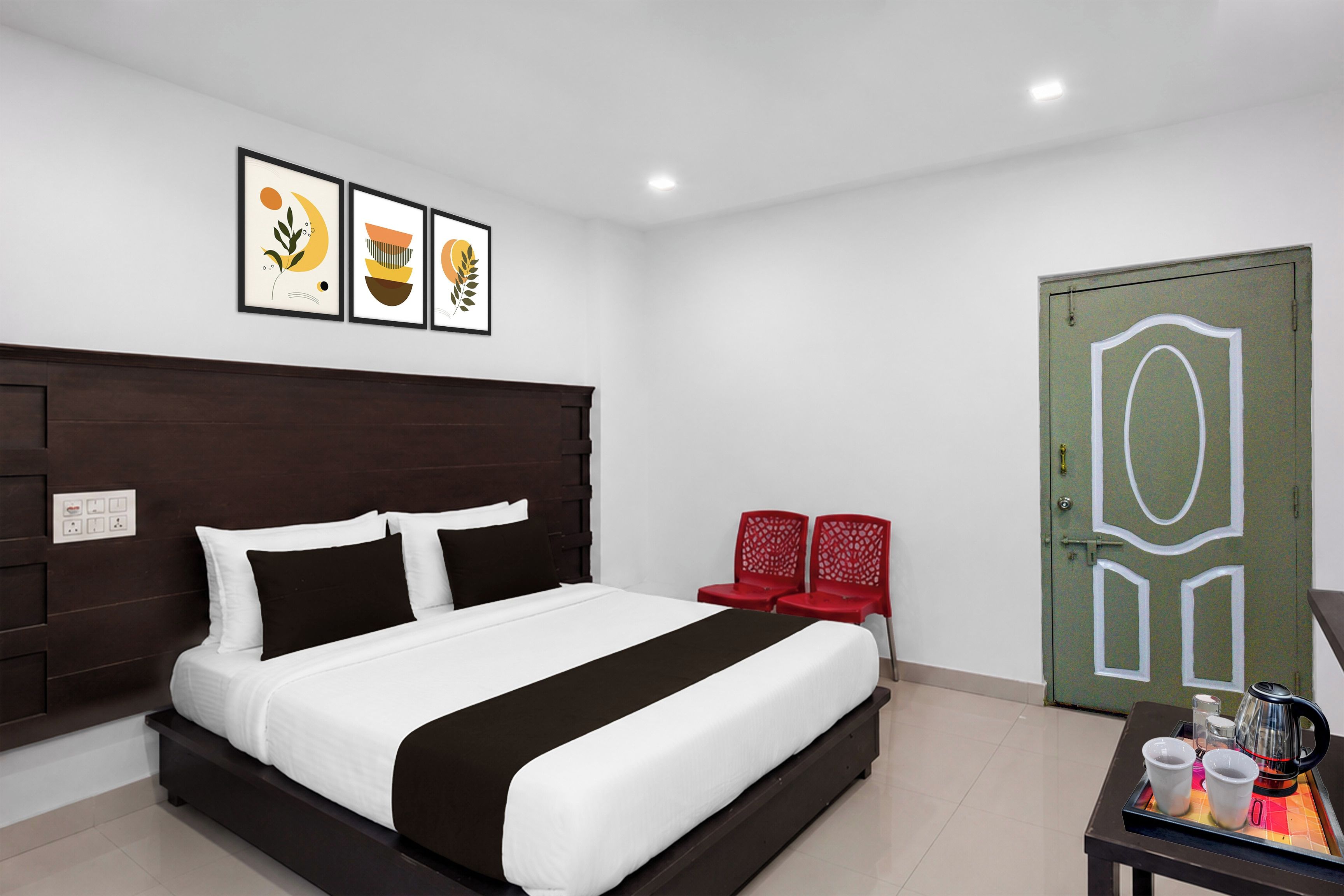 A modern hotel room with a large bed, a bedside table with two cups and a kettle, and a green door with a geometric design.