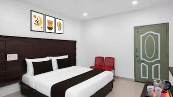 A modern hotel room with a large bed, a bedside table with two cups and a kettle, and a green door with a geometric design.