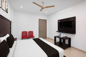 Una habitación de hotel con una cama, dos sillas rojas, un televisor y un ventilador de techo.