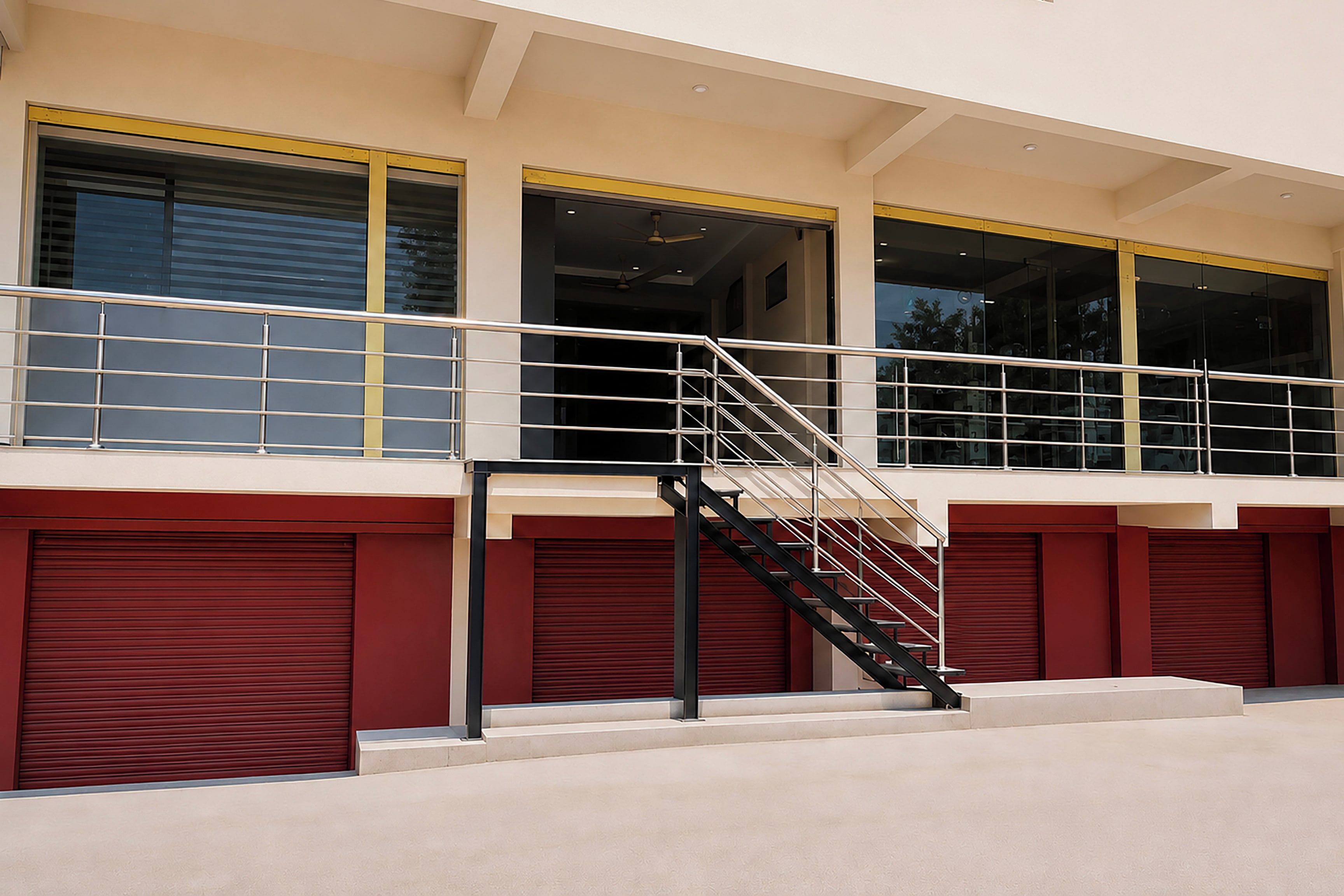 A building with a staircase leading to a balcony, large windows, and red garage doors.