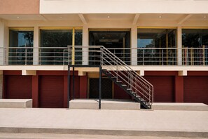 A building with a staircase leading to a balcony, large windows, and a garage door.