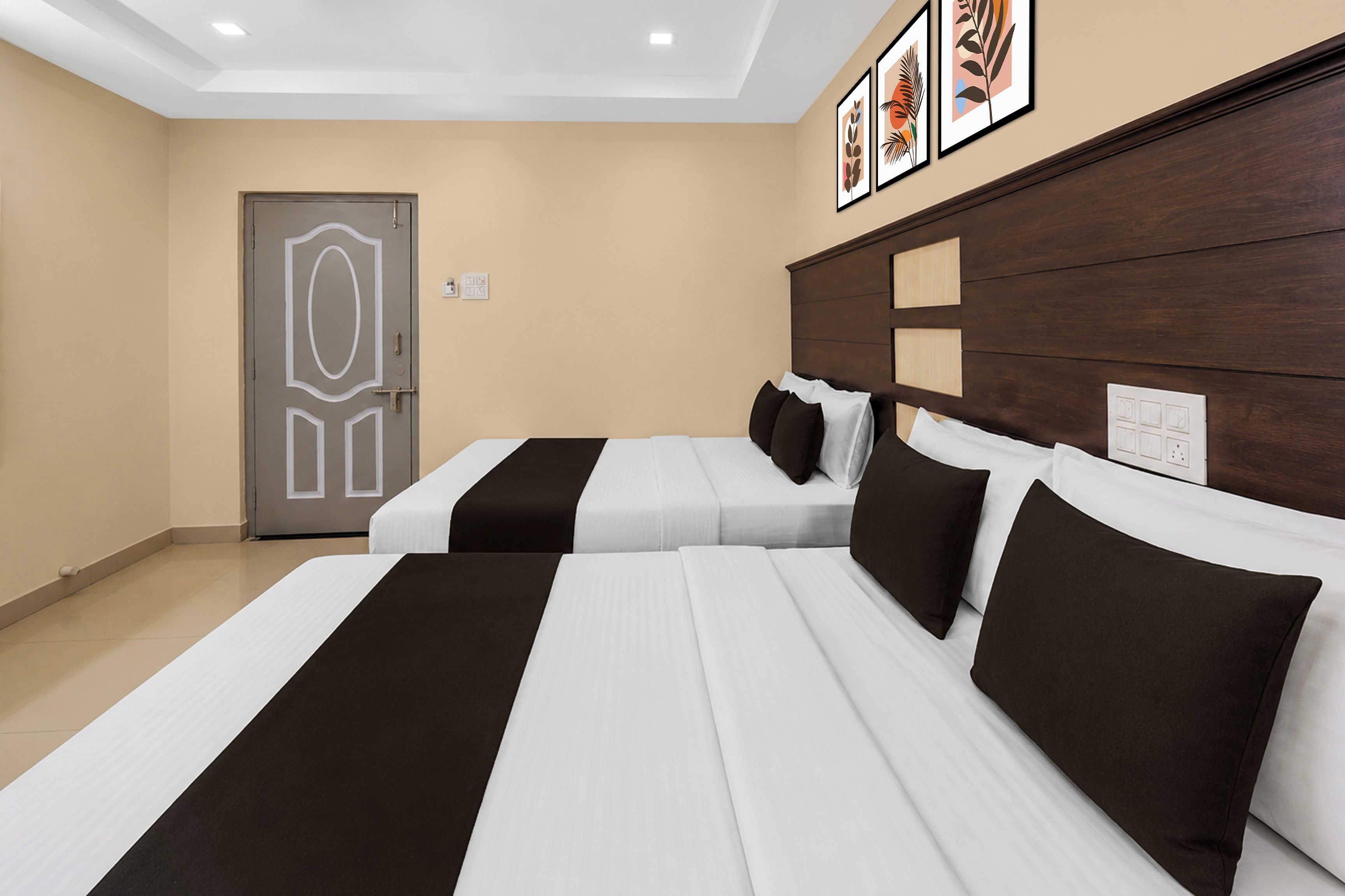 A hotel room with two beds, a wooden headboard, a door with a geometric design, and framed artwork on the wall.