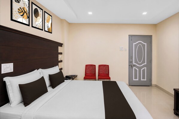 Une chambre d’hôtel avec un grand lit, deux fauteuils rouges, une porte ornée de motifs géométriques et des œuvres d’art accrochées au mur.