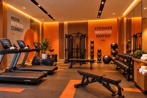 Un gimnasio con cintas de correr, banca para pesas y diferentes pesas.