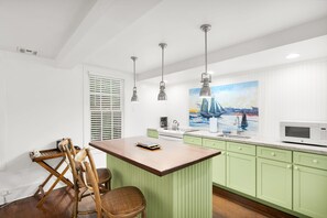 A kitchen with a wooden island, green cabinets, a painting of a sailboat, and a microwave. - Jacaranda Cottage 18+ Adult Only cottage near Duval St (Key West)