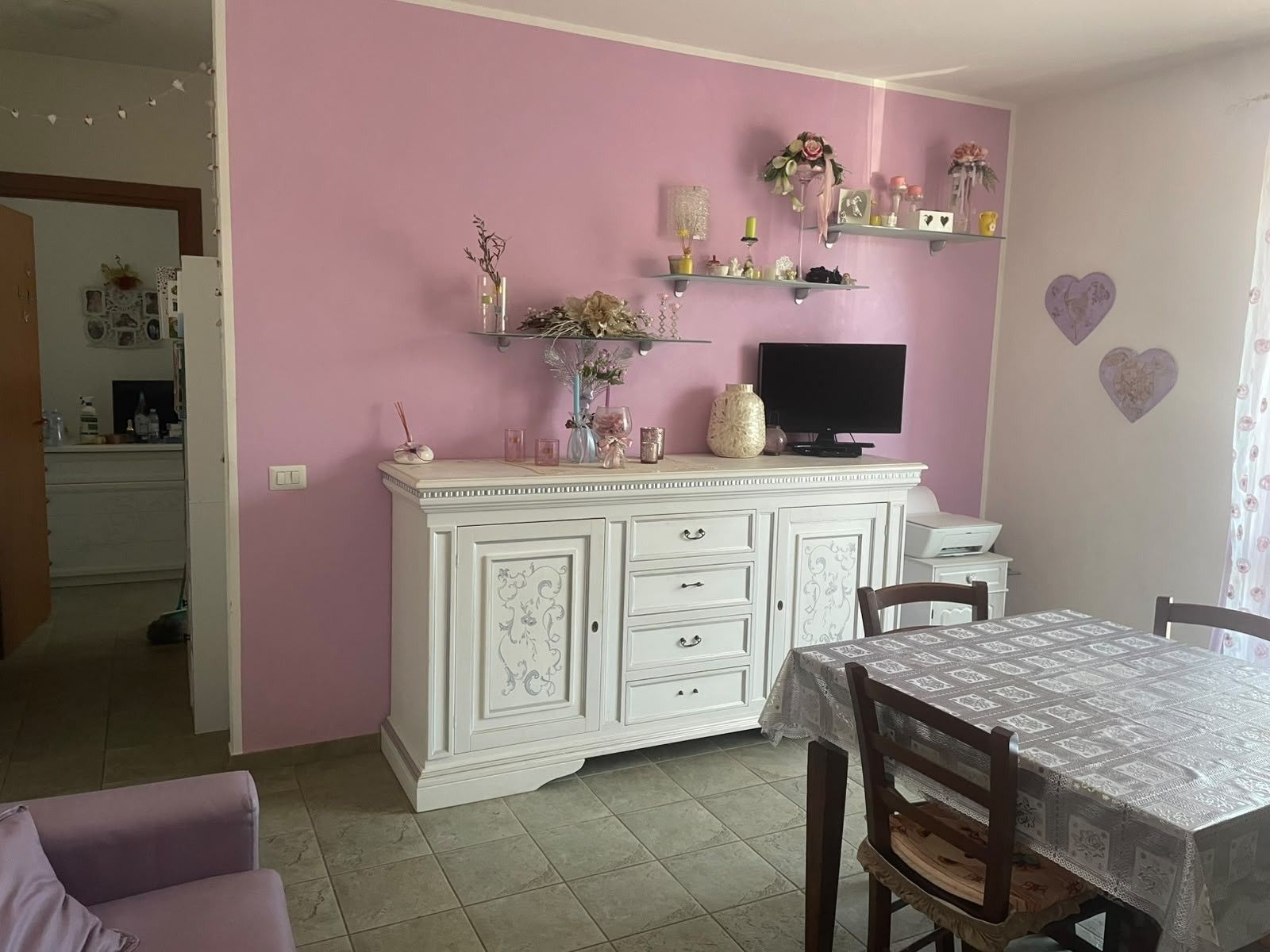 A dining area with a white cabinet, a television, and a table with a lace tablecloth.
