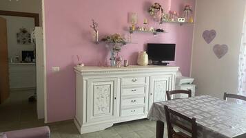 A dining area with a white cabinet, a television, and a table with a lace tablecloth.