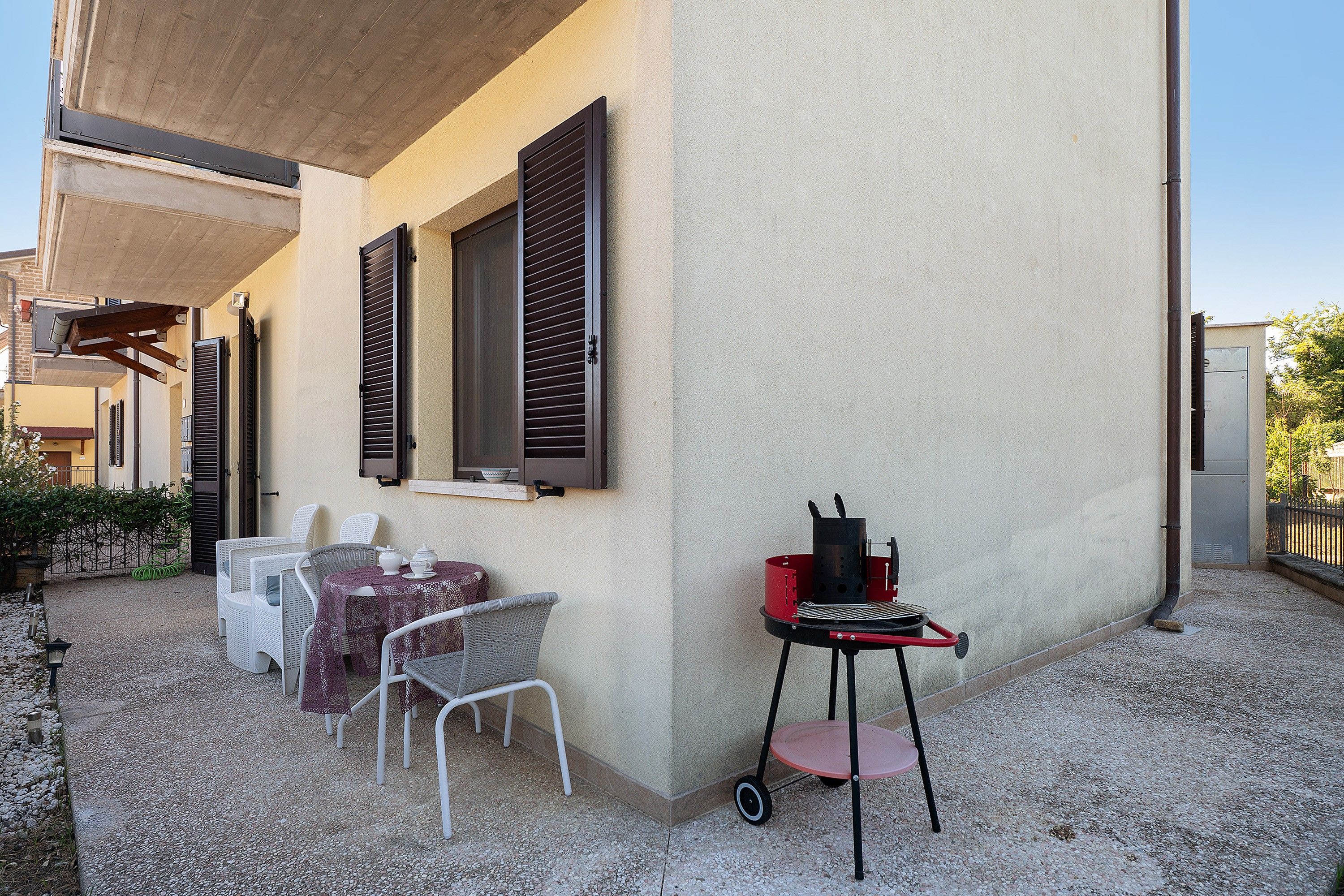An outdoor patio with a barbecue grill, outdoor seating, and a building with shutters.
