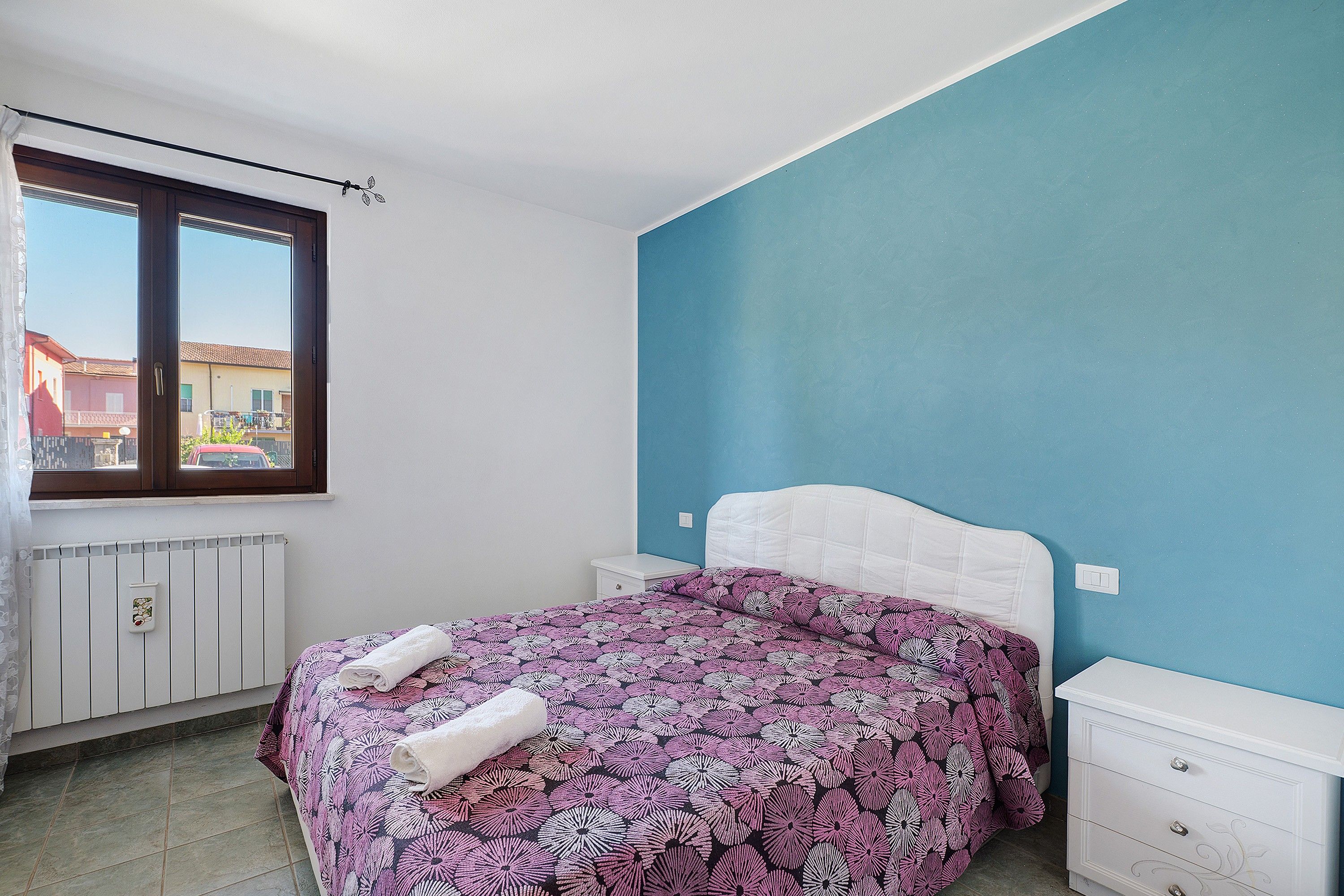 Una camera da letto con un letto, una finestra, un termosifone e un comò.