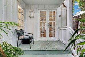 A porch with a bench, a white door with glass panels, and a small sign with the letters 'C6B'. - Frangipani Cottage  18+ Adult Only cottage near Duval St (Key West)