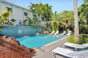A swimming pool with lounge chairs, palm trees, and a brick wall. - Frangipani Cottage  18+ Adult Only cottage near Duval St (Key West)