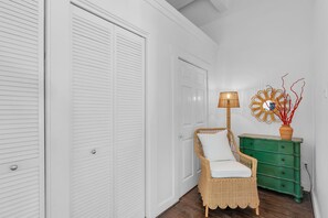 Ein Zimmer mit weißen Türen, ein Korbstuhl mit Kissen, eine grüne Kommode und eine Stehlampe.