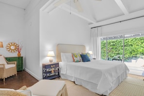 A bedroom with a bed, bedside lamps, a green dresser, a wicker chair, and a view of greenery outside. - Jasmine Manor 18+ Adult Only king retreats in a garden paradise (Key West)
