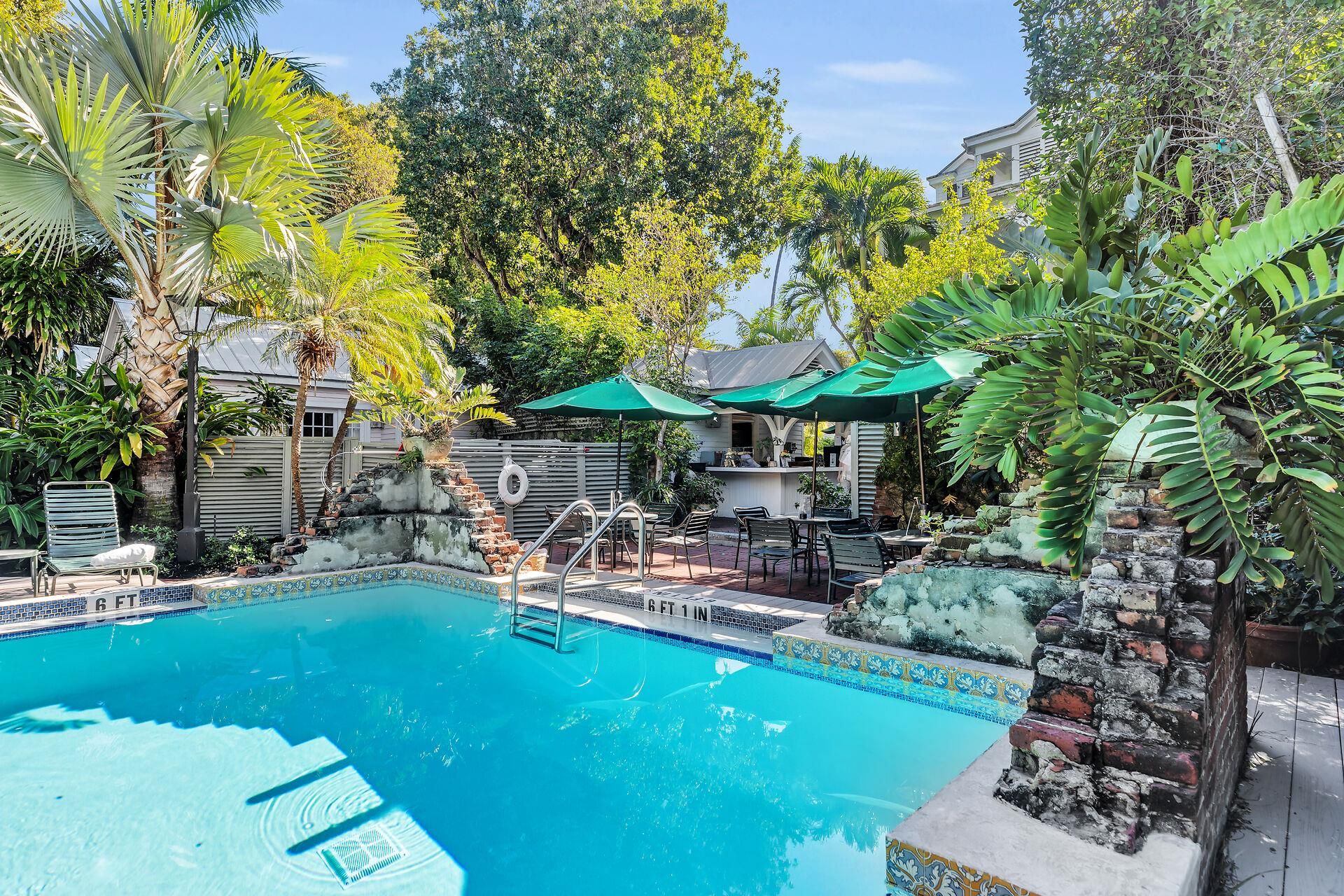 A swimming pool with a tiled edge, surrounded by greenery and outdoor furniture.