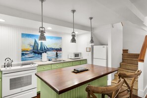 A kitchen with a wooden island, green cabinets, a white refrigerator, and a painting of sailboats. - Orchid Cottage, Two cottages, one 18+ Adult Only garden retreat (Key West)