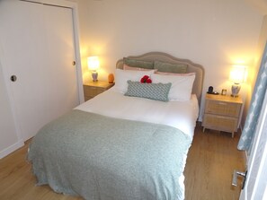 A neatly made bed with a grey blanket, two bedside tables with lamps, and a door. - Birnam Nook - 2 Bed cosy cottage 10 minute walk from Dunkeld. Pet Friendly. (Birnam)