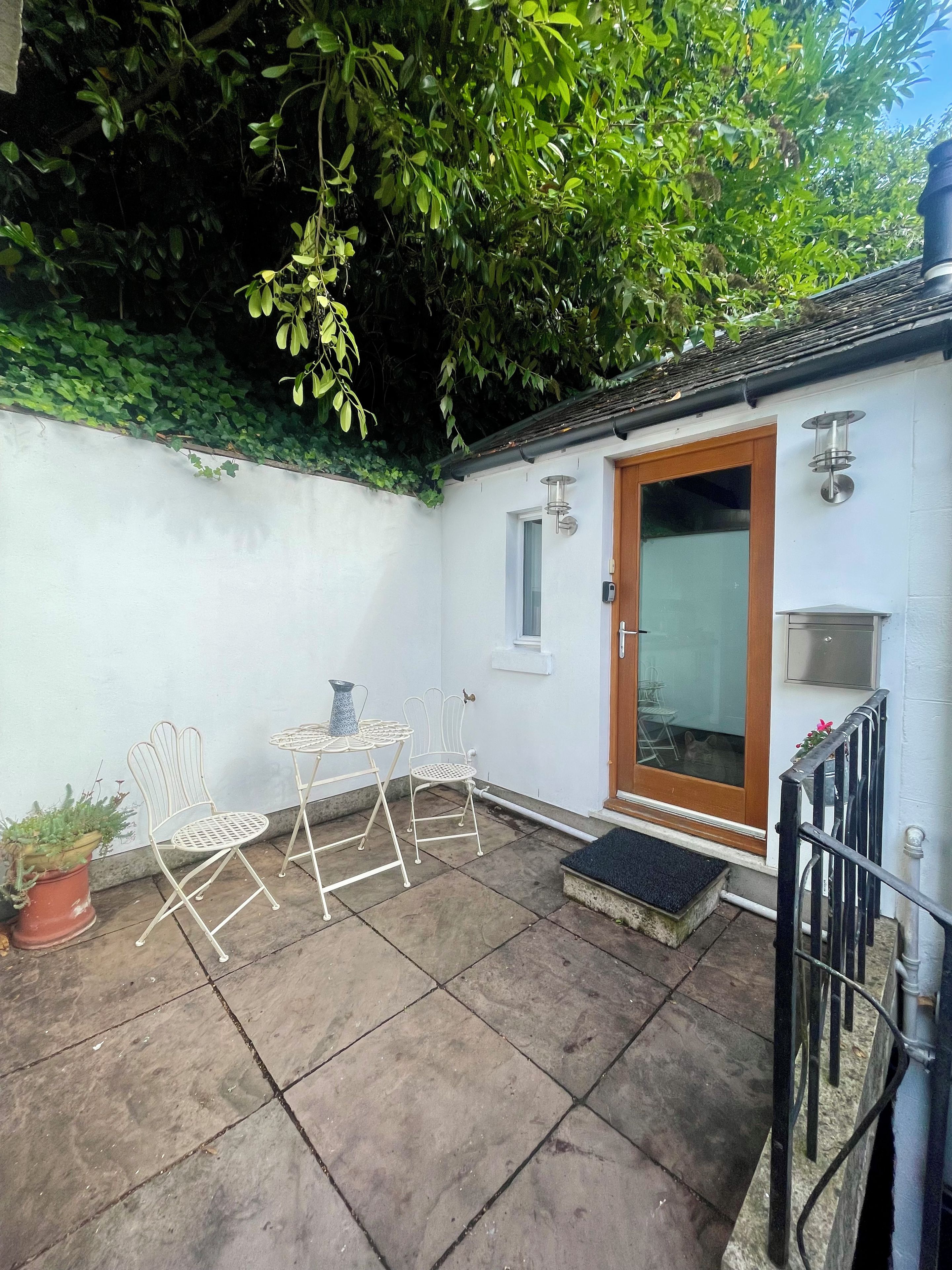 A patio with a white metal table and chairs, a potted plant, and a door with a window.