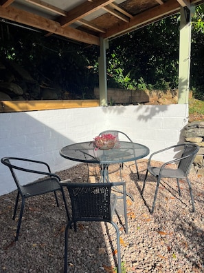An outdoor patio with a round metal table and four chairs, surrounded by pebbles and a white wall.