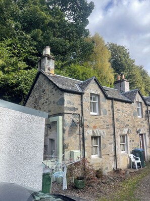 A stone building with multiple windows and a chimney. There is a white chair and a green trash bin outside. - Birnam Nook - 2 Bed cosy cottage 10 minute walk from Dunkeld. Pet Friendly. (Birnam)
