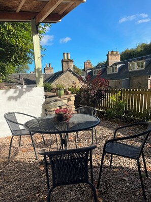 An outdoor patio with a round table and four chairs, surrounded by pebbles and plants. - Birnam Nook - 2 Bed cosy cottage 10 minute walk from Dunkeld. Pet Friendly. (Birnam)