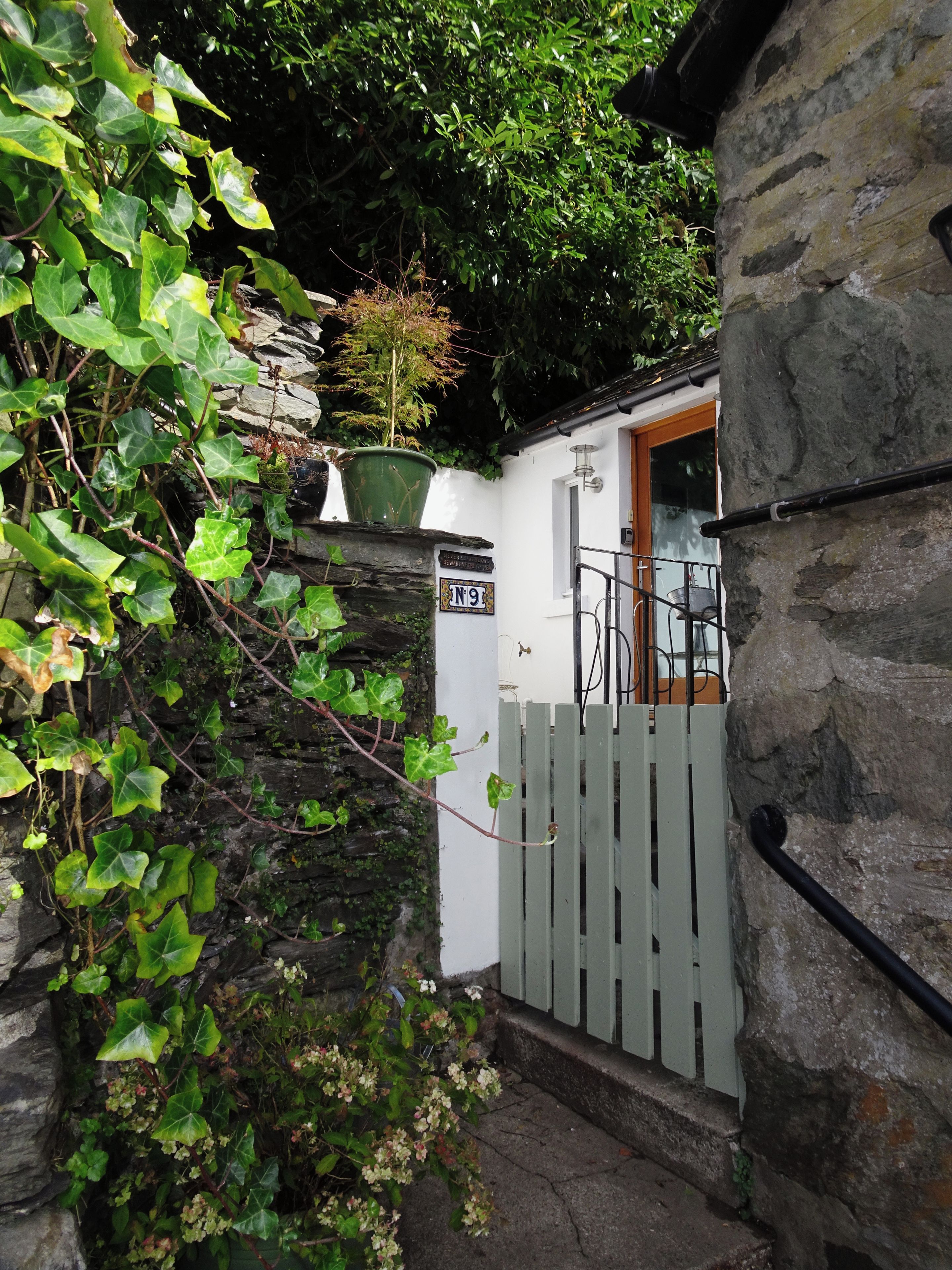 A stone wall with a wooden gate, a potted plant, and a sign with the number '9'.