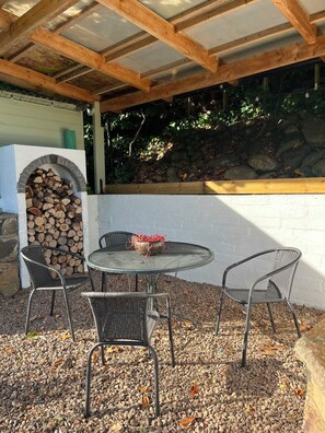 An outdoor patio with a round table and four chairs, a brick fireplace, and a stone wall. - Birnam Nook - 2 Bed cosy cottage 10 minute walk from Dunkeld. Pet Friendly. (Birnam)