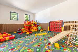 Ein Spielzimmer mit einer weichen Krabbeldecke, bunten Bauklötzen und einer kleinen Rutsche.
