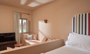 Ein Schlafzimmer mit Bett, Sofa, kleinem Tisch, einem Fenster mit Vorhängen und einer Wandleuchte.
