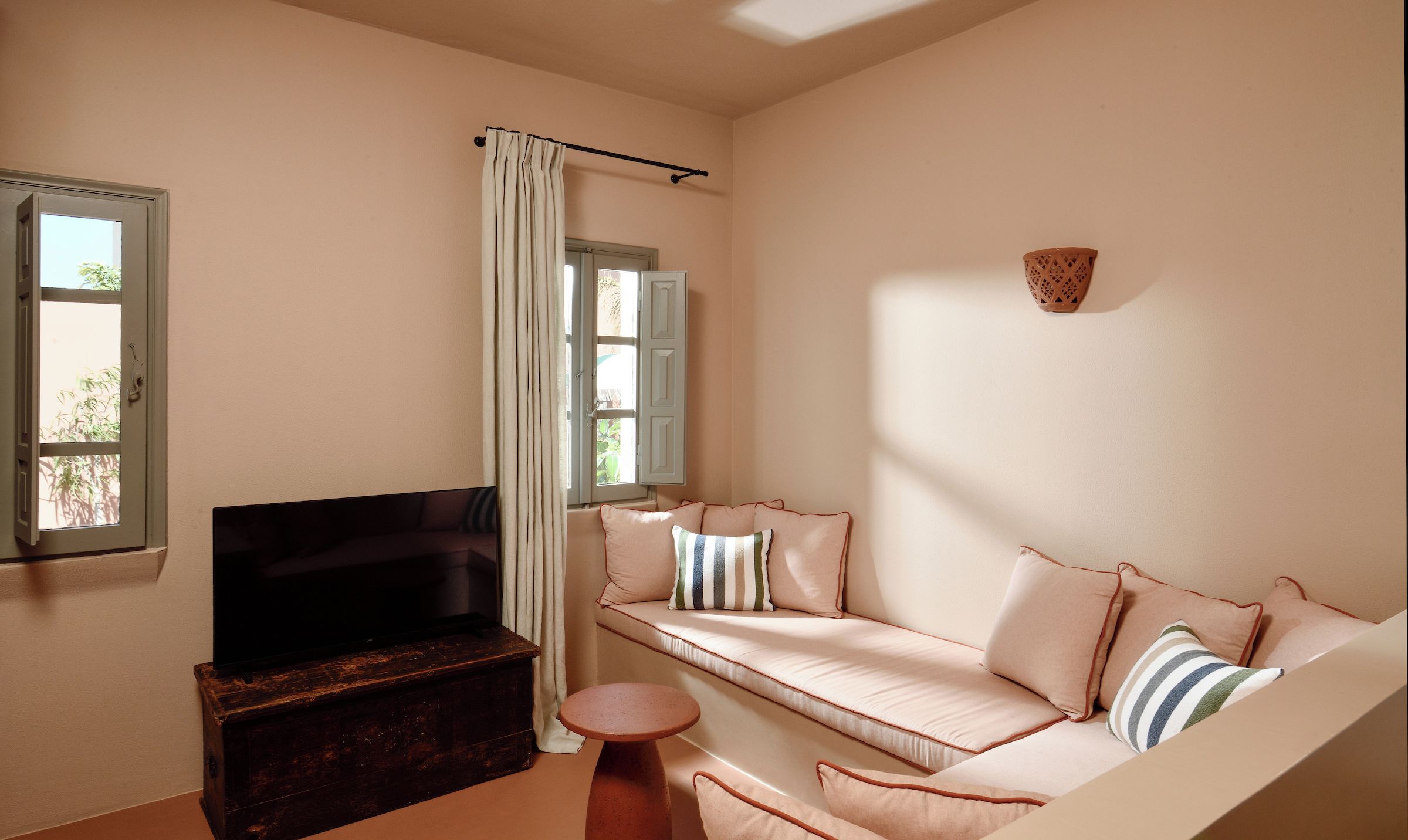 Una sala de estar con un sofá, un televisor, una mesita y una ventana con cortinas.
