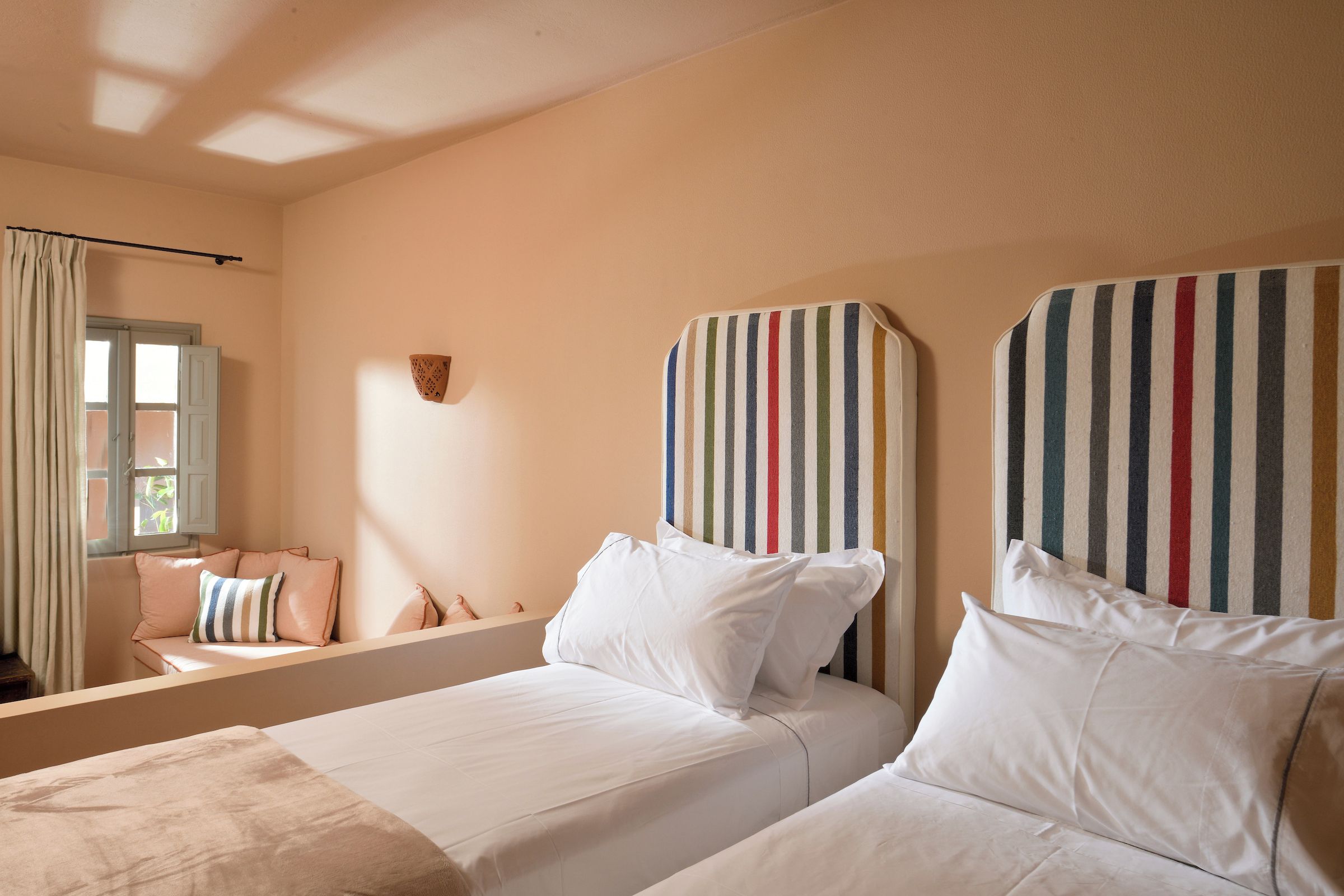 A bedroom with two beds, a window with curtains, and a striped headboard.