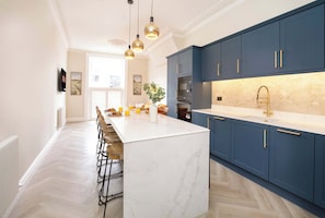 Una cocina moderna con una isla de mármol, armarios azules y una zona de bar con taburetes.