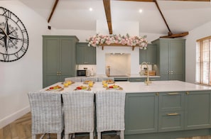 A kitchen with a central island, green cabinets, a decorative flower arrangement, and a large wall clock. - Ousegate Skyline Retreat, sleeps 6 (York)