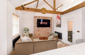 A living room with a brick wall, a flat-screen TV mounted on it, a sofa, a coffee table, and a plant. - Ousegate Skyline Retreat, sleeps 6 (York)