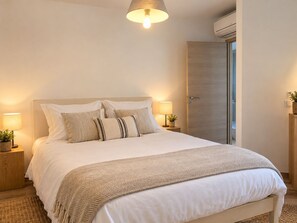 Un dormitorio con cama, lámparas de noche, mesita de noche, aire acondicionado de pared y una puerta.