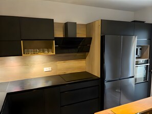 Eine moderne Küche mit einem schwarzen Kühlschrank, Holzschränken und einem eingebauten Backofen.