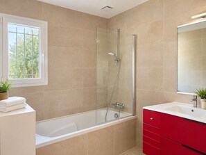Un baño moderno con ducha de vidrio, una bañera blanca y un tocador rojo con espejo.