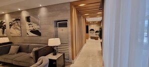 Ein modernes Wohnzimmer mit einer Couch, einem Beistelltisch und einer Lampe. An den Wänden befinden sich abstrakte Gemälde und ein Flur, der in einen anderen Raum führt.
