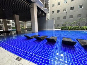 A modern indoor swimming pool with blue-tiled flooring and lounge chairs. - Modern Hotel-Style Condo Near MOA Arena & Mall of Asia and Dedicated Parking (Pasay City)