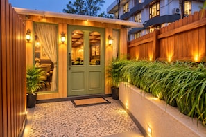 Une façade en bois avec une porte verte, des plantes en pot et un porche carrelé.
