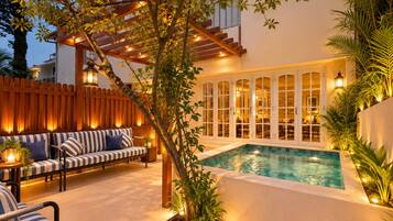 Un área de piscina con cubierta de madera, un sofá y una pérgola con luces.